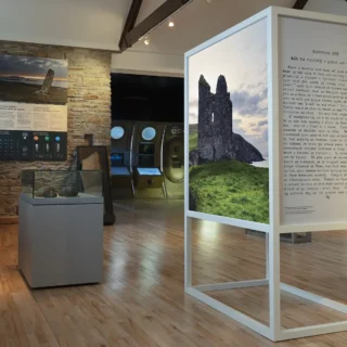 Selection of panels within the exhibition. The main focus is a photo of an old stone fort. In the background are more exhibits about the ocean and ogham stones.