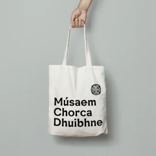 A white cotton tote bag featuring Músaem Chorca Dhuibhne logo.