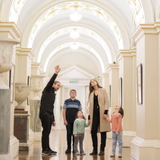 A family with young children exploring the halls of Dublin Castle. They are pointing and gazing at details on the ceiling.