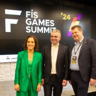 Alan Duggan, Dara Calleary and a woman in a green suit pose for a photo infront of a display at the Fís Games Summit 2024.