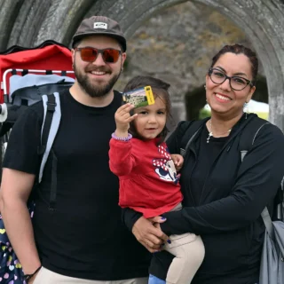 A family with a young child holding a Heritage Card, in the background is Clonmacnoise.