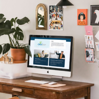 A desk with a MacBook screen displaying the professional learning page on the Teaching Council website. The desk also features a plant. There is an assortment of cards and pictures on the wall.