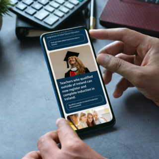 A person holds a smartphone displaying the Teaching Council website. The content on the screen highlights information for teachers who qualified outside of Ireland, indicating that they can now register and complete their induction in Ireland.