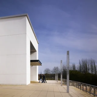 Exterior of a building made out of concrete slabs. There are three people walking in the entrance.