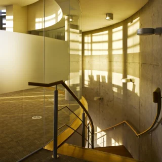 A stairwell interior in a building with sunlight shinning through glass panels onto a solid concrete wall.