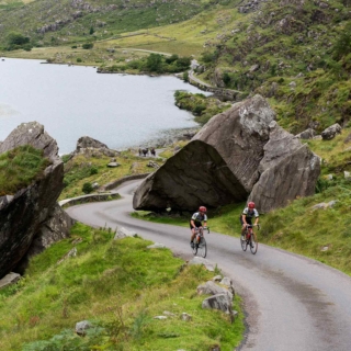 Two cyclists approaching a picturesque climb with a lake in the background and horse and cart.