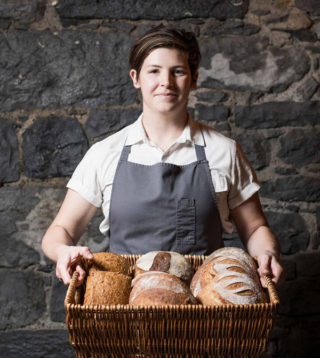 Portrait of a baker holding a basket of different types of freshly baked loaves of bread.