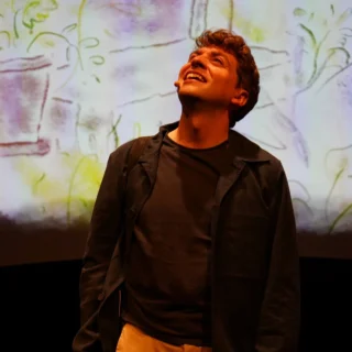 Performer on stage with microphone headset looking upwards against a colourful projected background