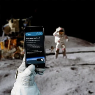 404 page of the ESERO website displayed on an iPhone. It is being held by an astronaut, in the background is an astronaut landing on the moon.