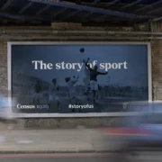 Census 1926 outdoor billboard reading 'The story of sport', featuring a black and white photograph of a GAA match, displayed on a brick wall under a railway bridge.