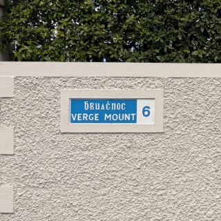 A blue bilingual street sign with Cló Gaelach for the Irish text and Roman letterforms for the English text. The sign dates to the 1950s.