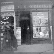 Photographic print of Irish Republican and rebel Thomas Clarke leaning against the door of his shop under a sign painted in Irish lettering ca. 1890-1916. (Courtesy of the National Library of Ireland)
